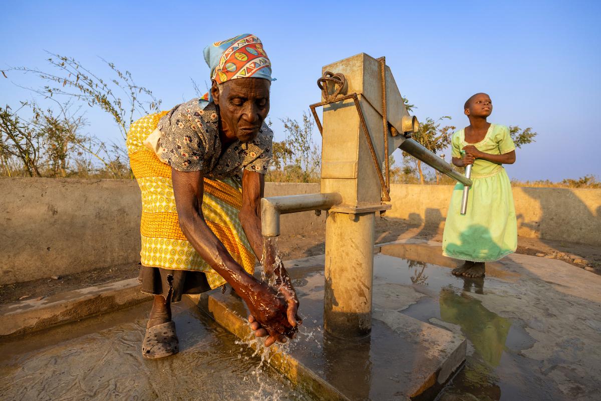 Vrouw wast haar handen bij een waterpomp